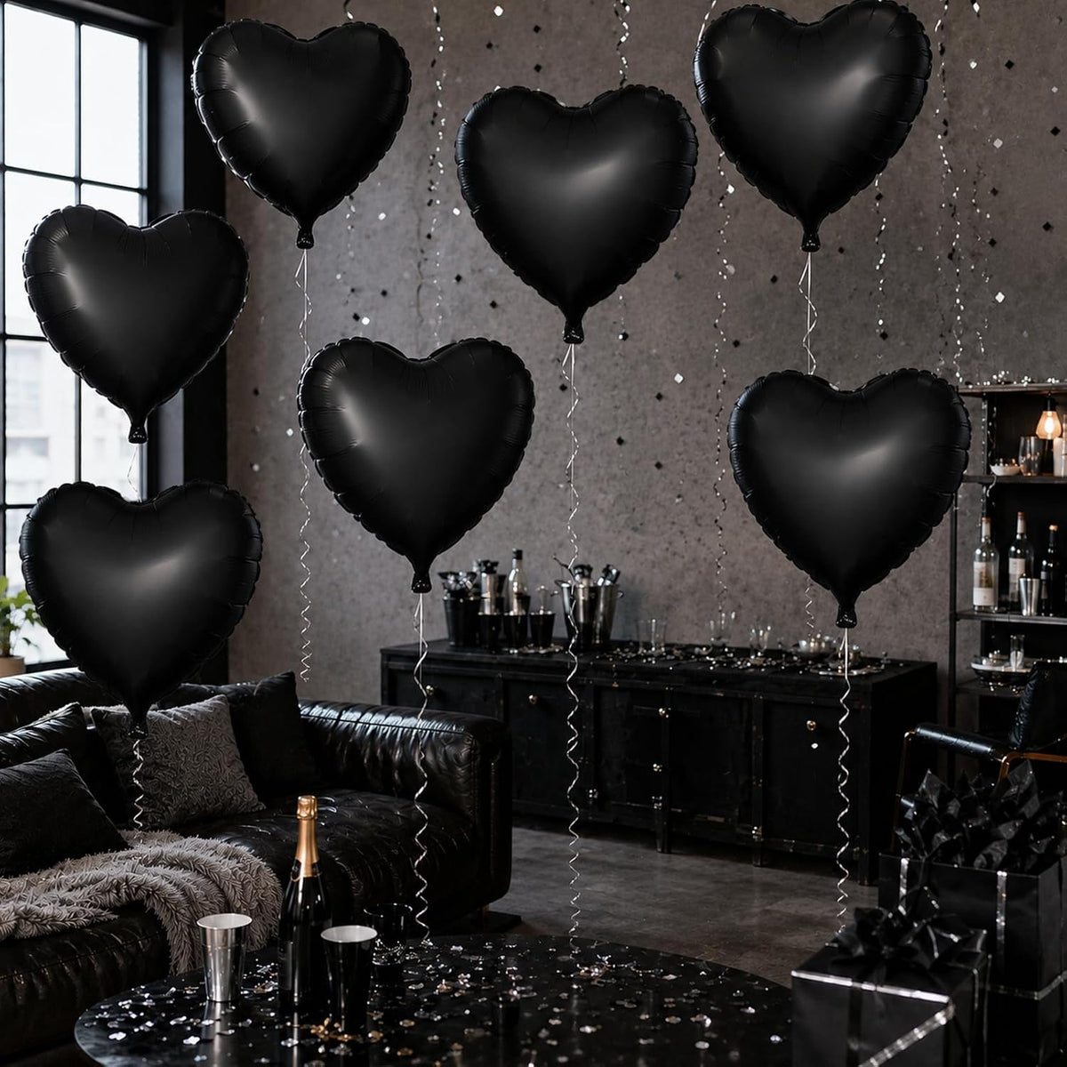 Six black heart-shaped foil balloons floating in a dark, stylishly decorated room with a black leather couch, a black bar cabinet, and a glittery gray wall.