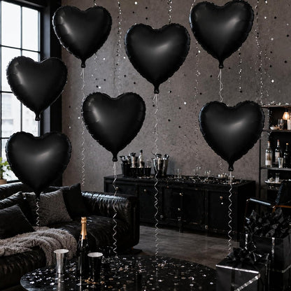 Six black heart-shaped foil balloons floating in a dark, stylishly decorated room with a black leather couch, a black bar cabinet, and a glittery gray wall.