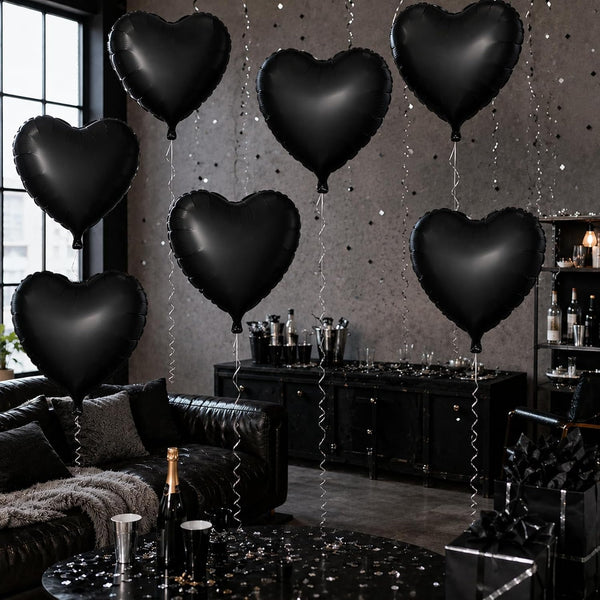 Six black heart-shaped foil balloons floating in a dark, stylishly decorated room with a black leather couch, a black bar cabinet, and a glittery gray wall.