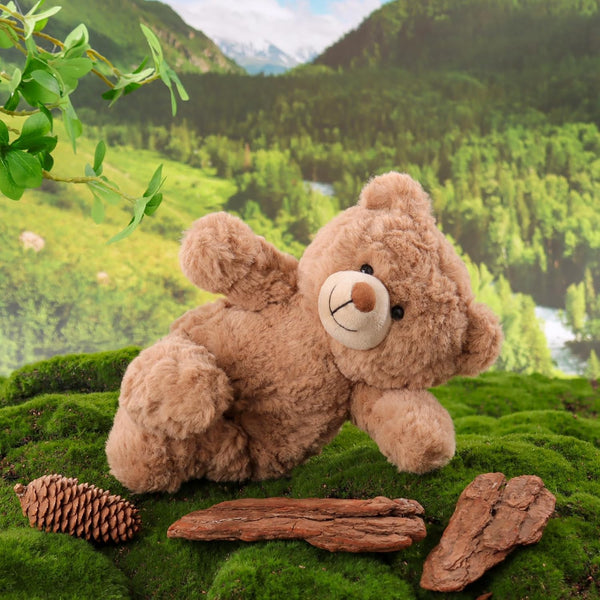 Teddy bear on a mossy rock with a scenic background of trees and mountains.