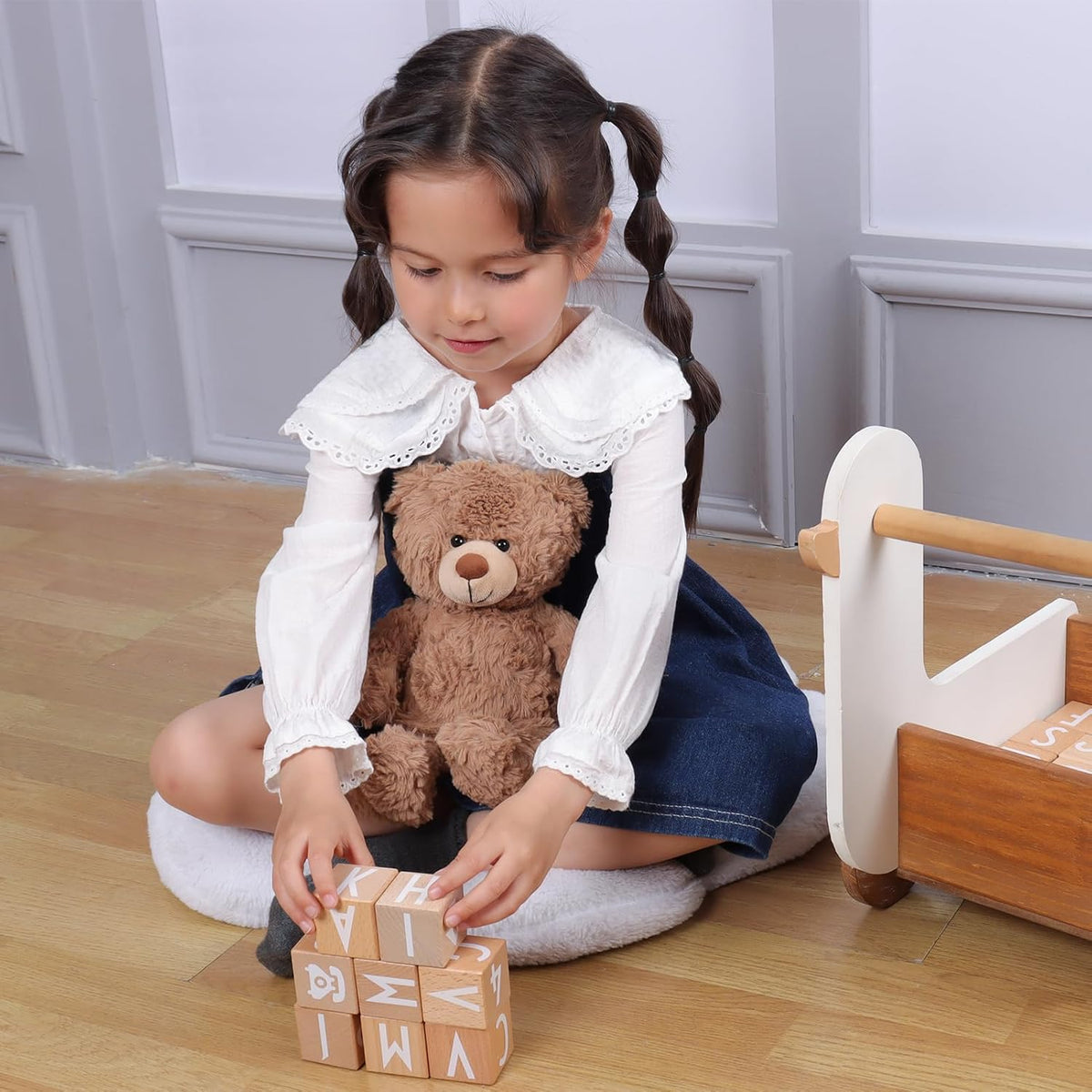 Child playing with blocks and a teddy bear on a wooden floor.