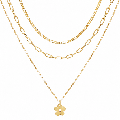 A gold layered necklace set featuring three distinct chain styles: a delicate cable chain, a medium Figaro chain, and a fine paperclip chain with a small five-petal flower pendant, shown against a solid white background.