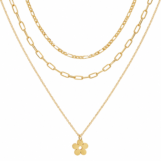A gold layered necklace set featuring three distinct chain styles: a delicate cable chain, a medium Figaro chain, and a fine paperclip chain with a small five-petal flower pendant, shown against a solid white background.