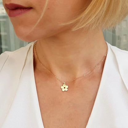 A close-up of a woman wearing a delicate gold chain necklace with a small flower-shaped pendant, paired with a white blazer.