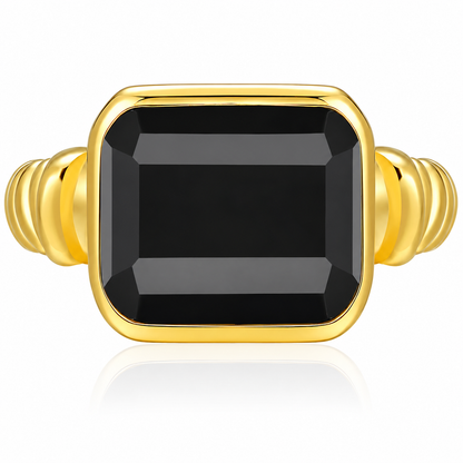 A gold ring featuring a large, faceted rectangular black gemstone in a bezel setting, with a ribbed gold band on a clean white background.