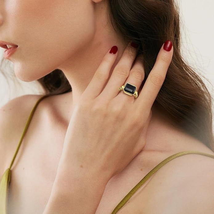A close-up lifestyle shot of a model wearing a gold signet ring with a rectangular black stone on her finger.